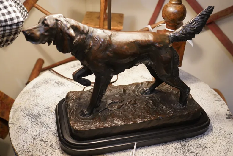 A bronze sculpture of a setter with its tail raised, mounted on a shaped black plinth on a distressed white round table.