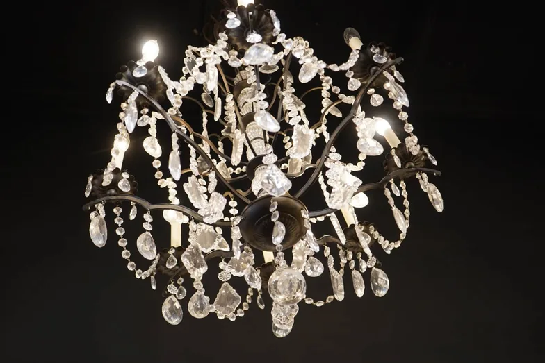 A crystal-and-bronze chandelier photographed against a dark wall, its beaded swags and cut prisms lit from within.