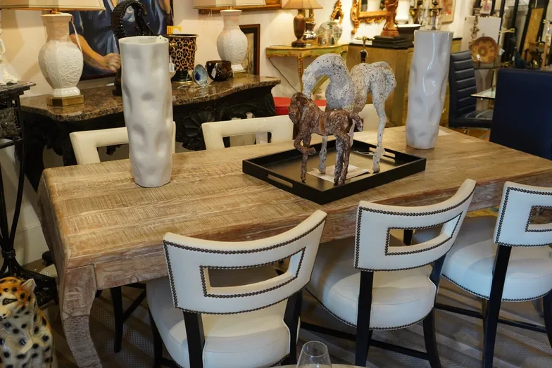 A light reclaimed-wood dining table with cream leather and black-framed chairs, styled with tall white ceramic vases and a carved horse figure on a black tray.
