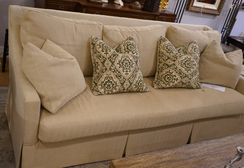 A cream skirted three-cushion sofa in a herringbone weave with two green-and-white patterned throw pillows.